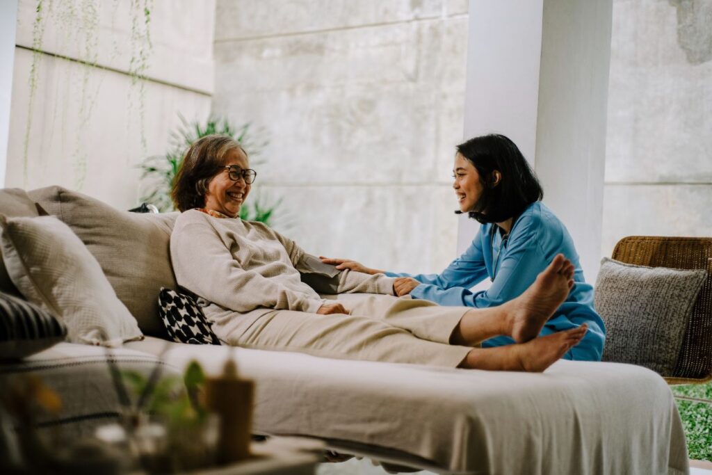 female caregiver helping an elderly woman off the couch to do light exercise
