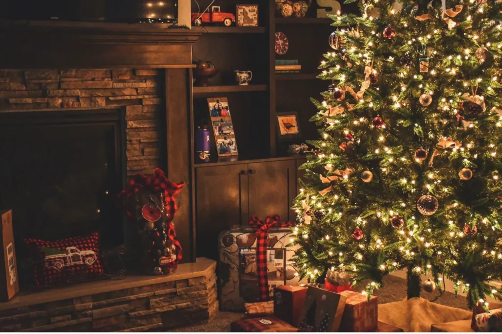 A Christmas tree in a living room with a presents below it and a brick fireplace net to it